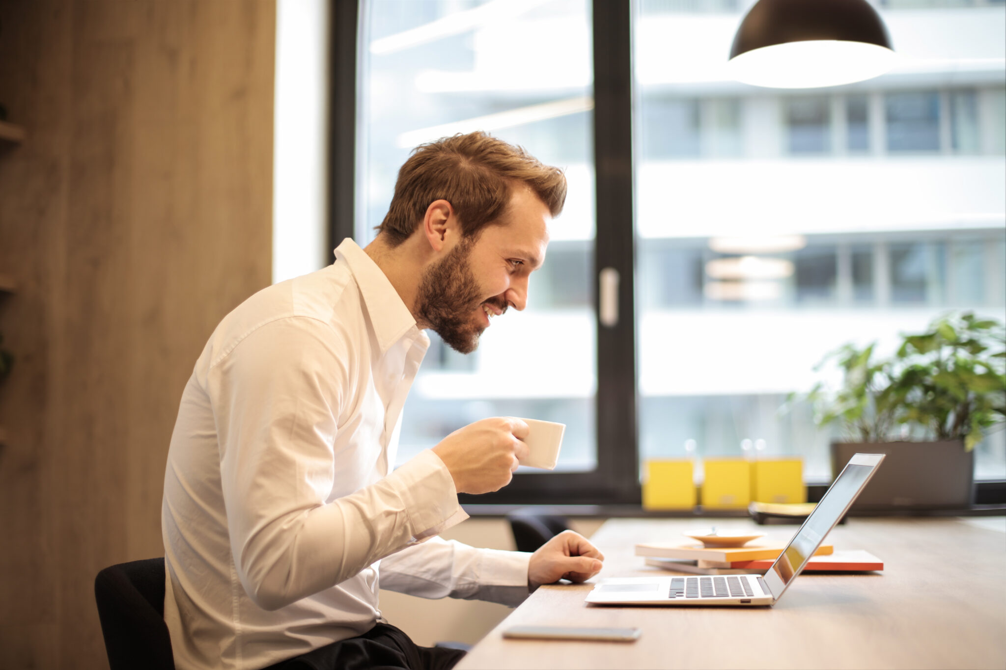 Man holding teacup infront of laptop on top of table inside the room